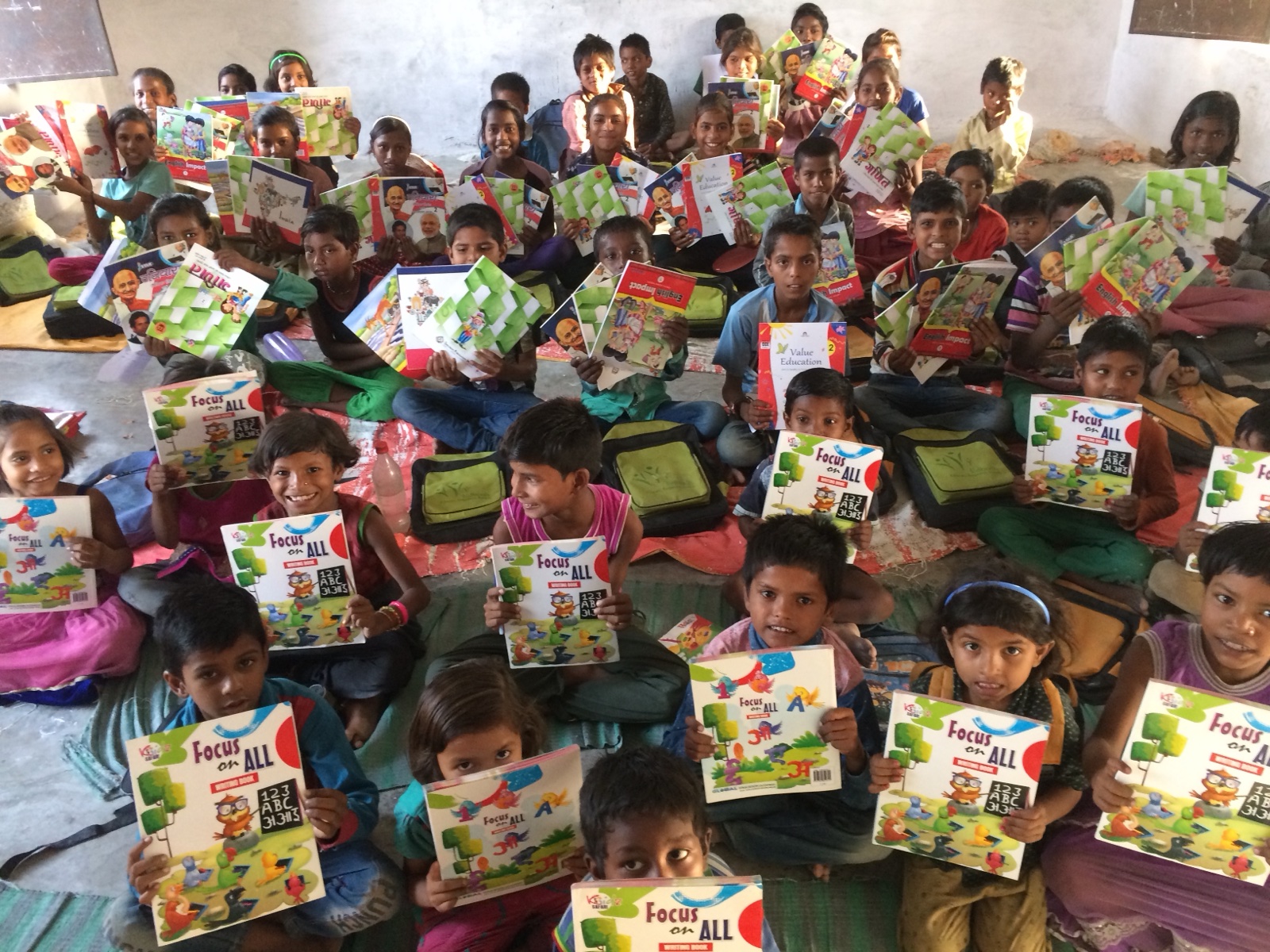 A full classroom of children in Masauli proudly holding their new book kits